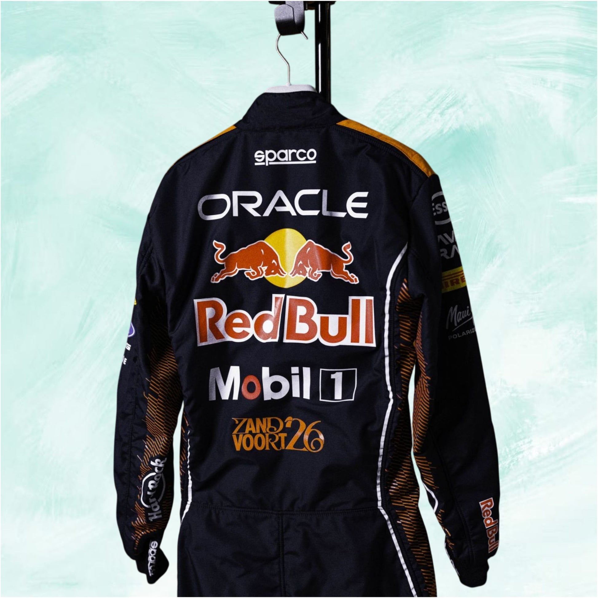 A black Red Bull Racing jumpsuit shown from the back, hanging on a black hanger against a light mint green textured background. The suit features prominent sponsor logos including Oracle, Red Bull, Mobil 1, Sparco, and Zandvoort 26.
